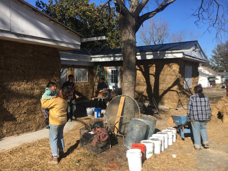 Several individuals in front of Magnolia house, which is wrapped in strawbales and being prepared for stucco. One is playing with a child.