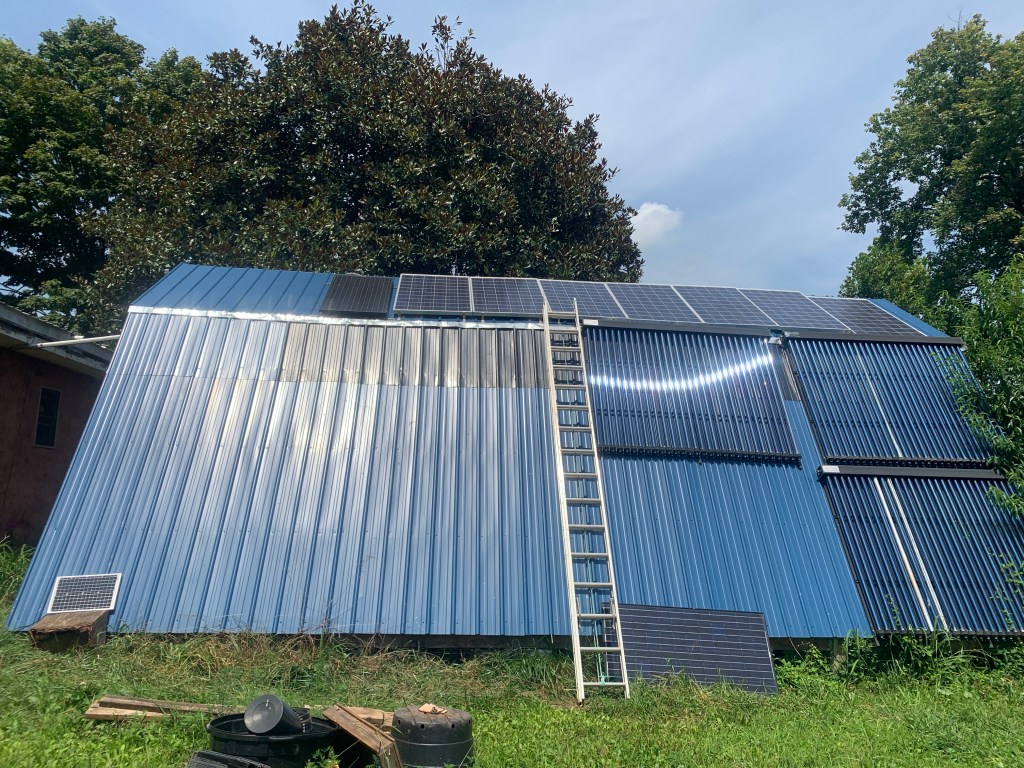 Magnolia shed with steeply slanted metal roof, a PV solar array, and a few vacuum tube solar thermal panels