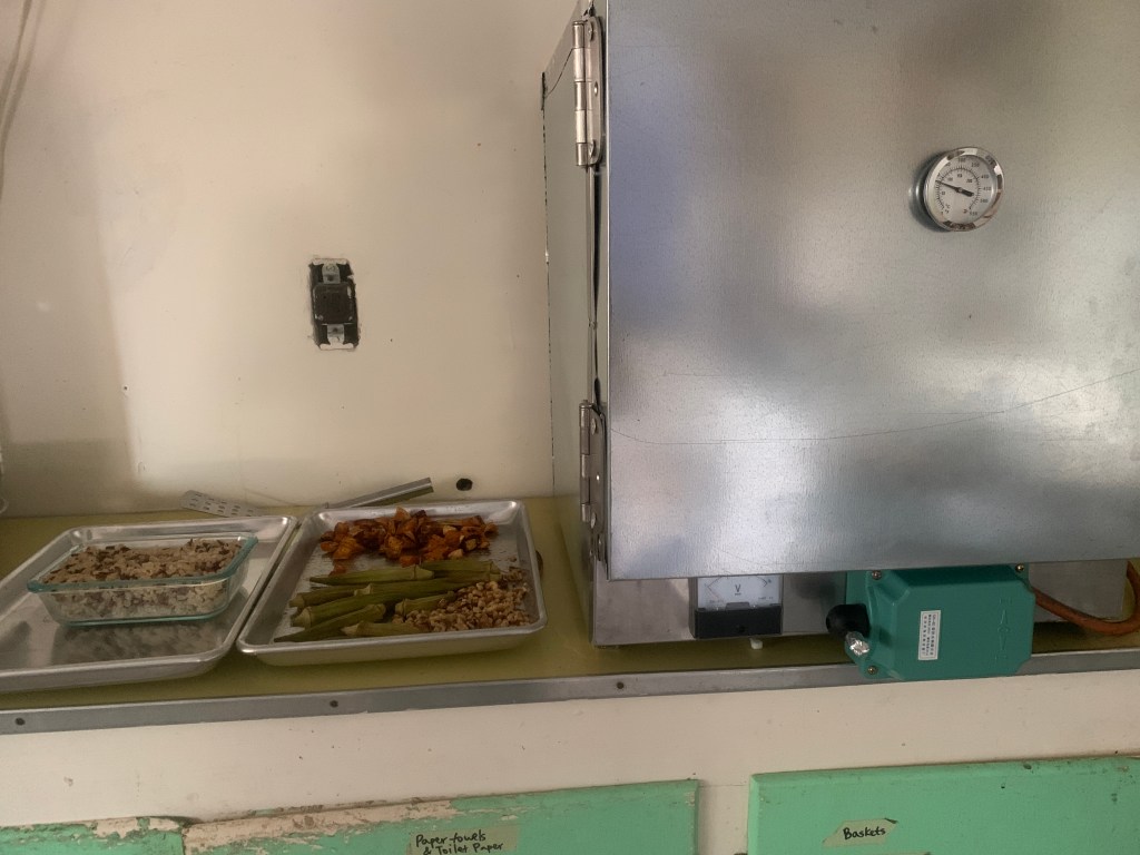 "Roxy" insulated solar cooker with trays of baked food beside it