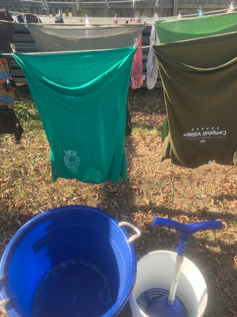 Clothes drying on line with laundry plunger and bucket in front